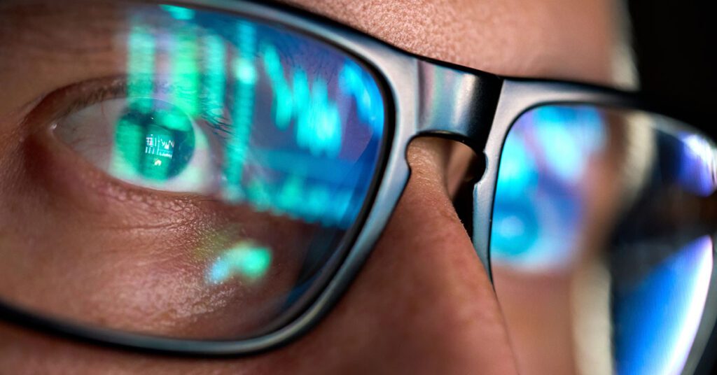 Close-up of a person wearing glasses with stock market graphs reflected in the lenses, symbolizing focus on risk management in investing.