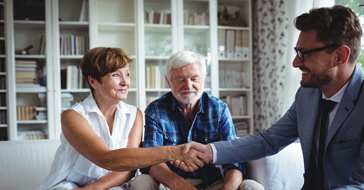 Financial advisor warmly shaking hands with a smiling couple in a comfortable, home-like setting—representing the human connection Financial Gravity empowers advisors to build.