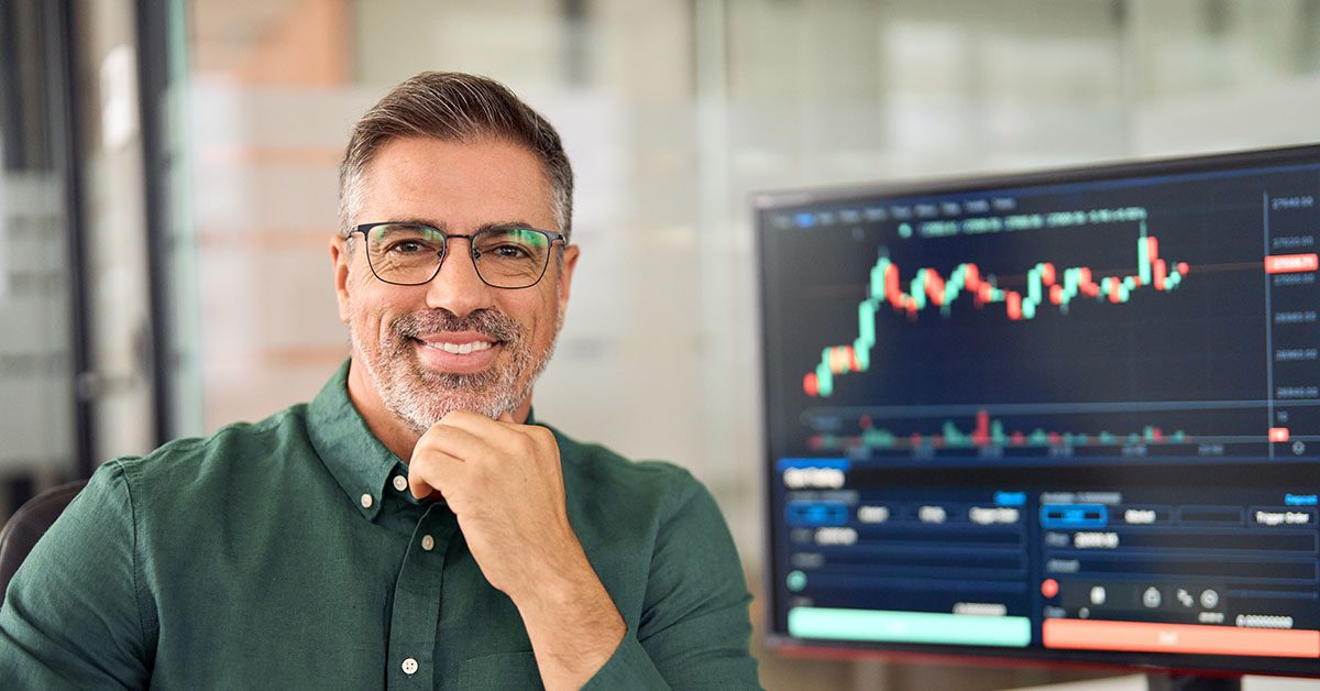 Confident financial professional smiling at his desk with a digital stock chart on the screen, symbolizing advisor expertise and strategic specialization in the AI era.