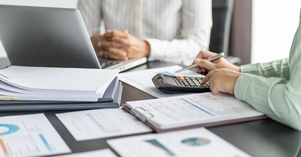 Advisor reviews risk reports with a calculator and laptop during a client meeting—Financial Gravity’s Turnkey Multi-Family Office Charter helps advisors manage tax, estate, and behavioral risks beyond market volatility.