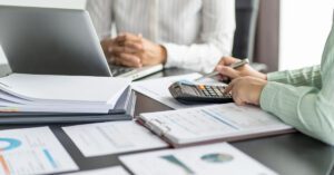Advisor reviews risk reports with a calculator and laptop during a client meeting—Financial Gravity’s Turnkey Multi-Family Office Charter helps advisors manage tax, estate, and behavioral risks beyond market volatility.