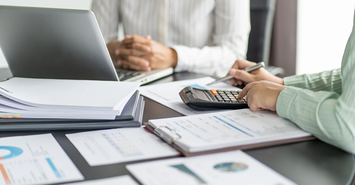 Advisor reviews risk reports with a calculator and laptop during a client meeting—Financial Gravity’s Turnkey Multi-Family Office Charter helps advisors manage tax, estate, and behavioral risks beyond market volatility.