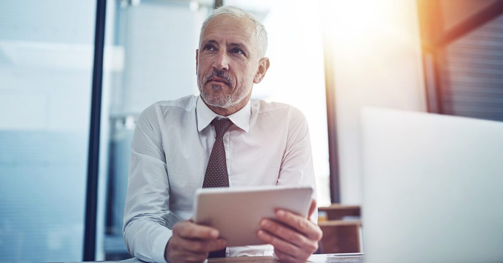 Financial Gravity equips financial advisors for a 10X mindset, shown by an executive reflecting with a tablet in a sunlit office.