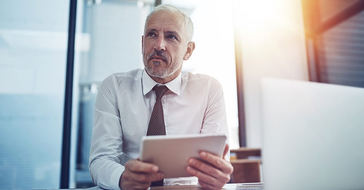 Financial Gravity equips financial advisors for a 10X mindset, shown by an executive reflecting with a tablet in a sunlit office.