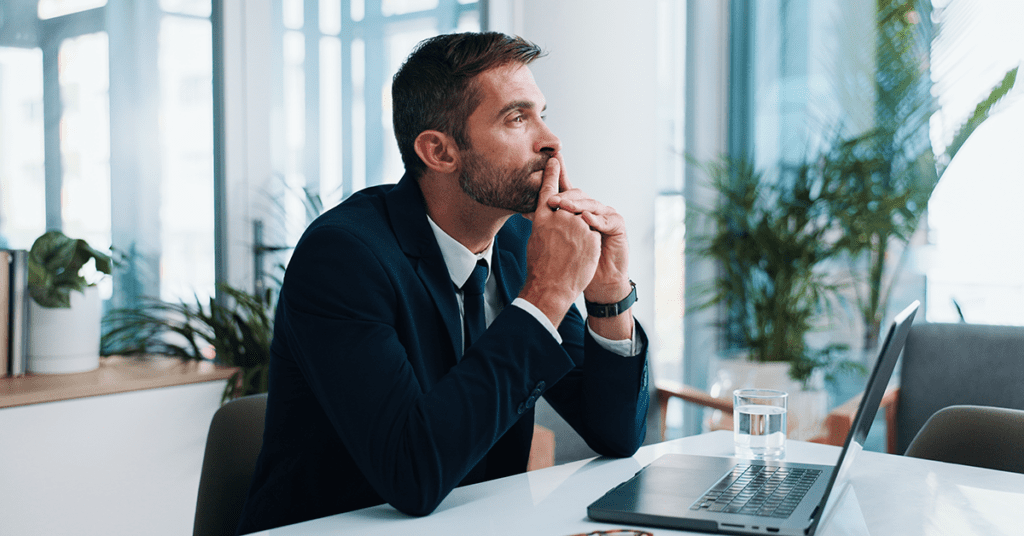 A focused financial advisor sits at a desk reviewing strategy on a laptop in a modern office setting.