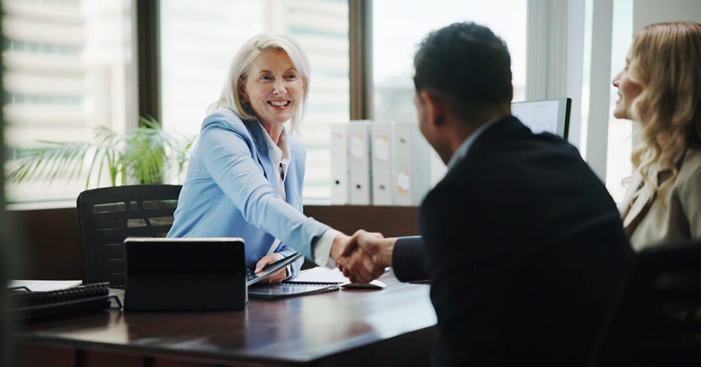 A financial advisor shakes hands with clients across a desk during a meeting in a professional office setting.