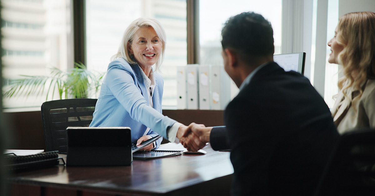 A financial advisor shakes hands with clients across a desk during a meeting in a professional office setting.