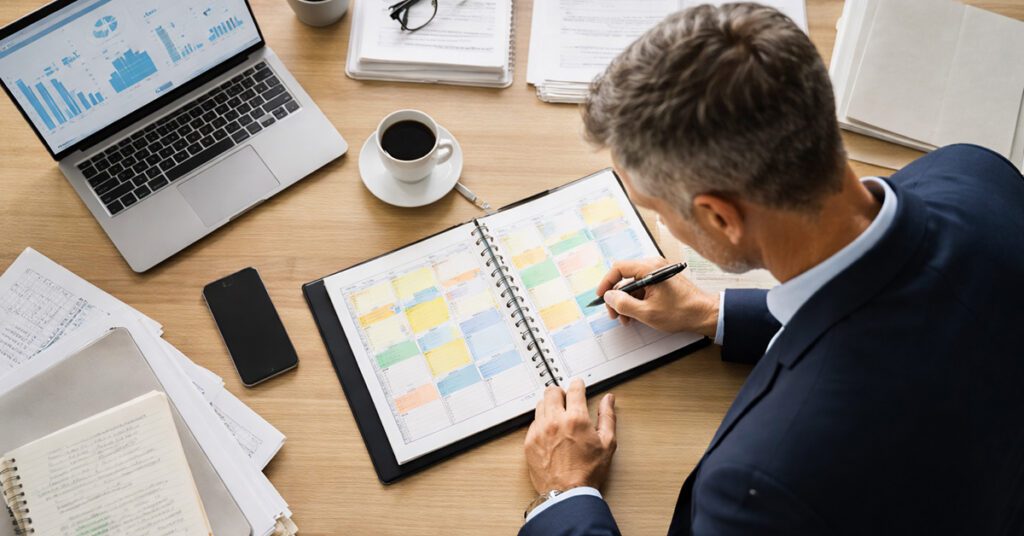 A financial advisor reviews and organizes a color coded weekly calendar and planning materials at a desk while preparing priorities for the week.